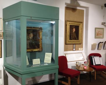 A museum display case displaying paintings of a world war 1 soldier by the artsit Stanhope Forbes