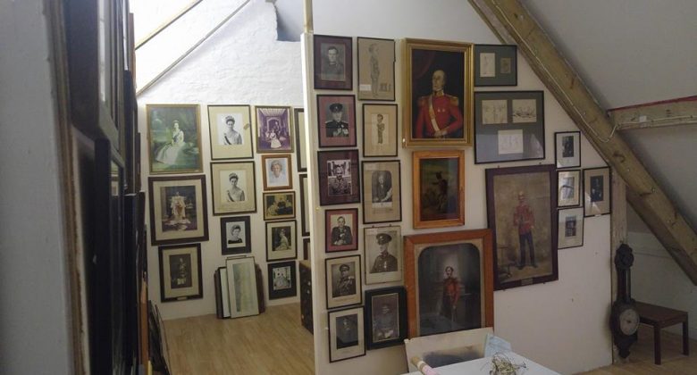 A light attic room with old pictures, portraits and photographs of various sizes, shapes and colours hanging from floor to ceiling