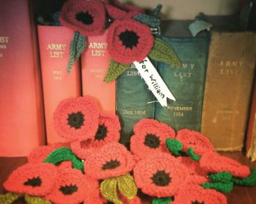 Twenty bright red handmade Poppies for Cornwall's Regimental Museum arranged against some WW1 era books in the library