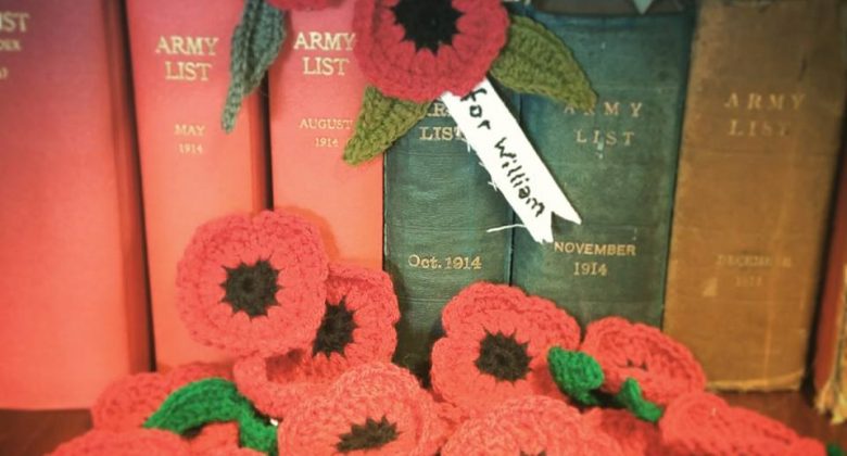 Twenty bright red handmade Poppies for Cornwall's Regimental Museum arranged against some WW1 era books in the library