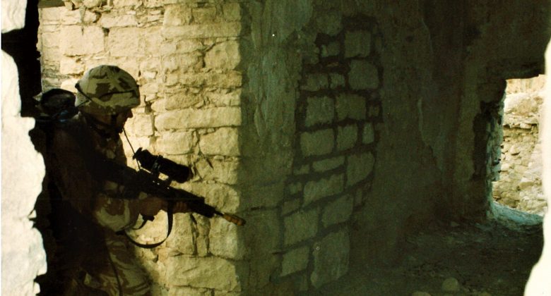 Photograph of soldier with their gun at the ready, entering a ruined building.